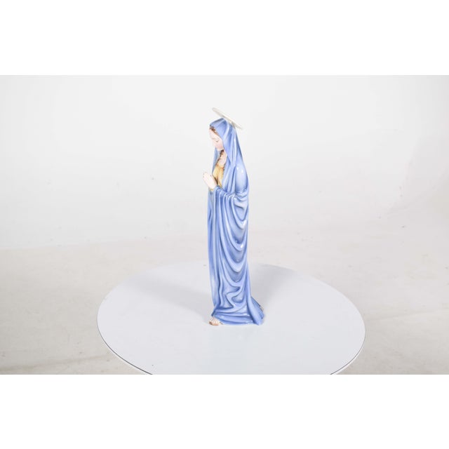 Image of a saint in pottery, with a crown and clasped hands. An angelic face looking down, she is covered by a beautiful...