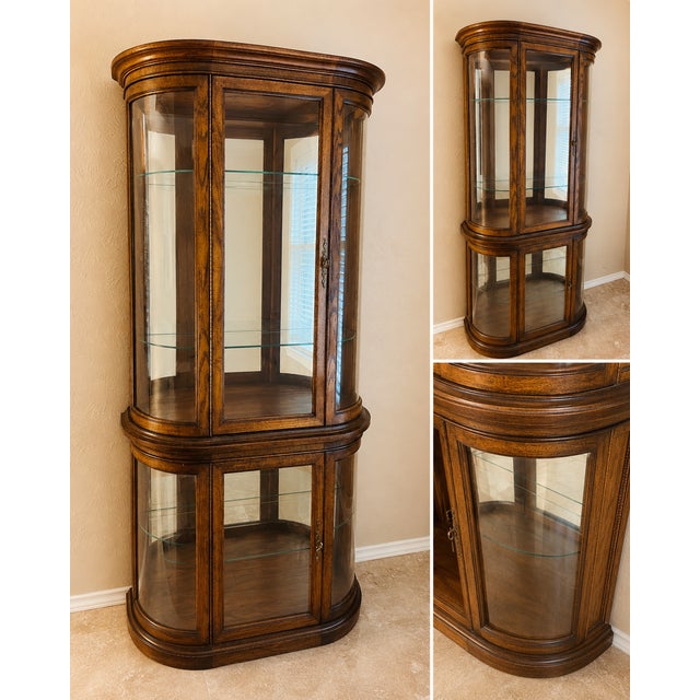 An elegant vintage illuminated curio cabinet featuring graceful curved glass panels, richly figured walnut veneers, and a...