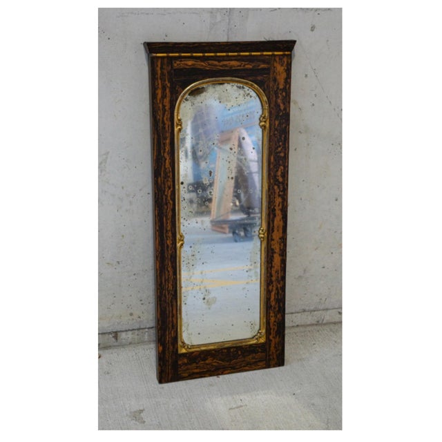 A tall, narrow rectangular mirror in faux tortoiseshell wooden frame in rich wood grain browns and black with a thin gilt-...