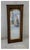 A tall, narrow rectangular mirror in faux tortoiseshell wooden frame in rich wood grain browns and black with a thin gilt-...
