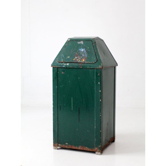 This vintage metal swing-top trash can, circa 1950s–1960s, features a tall architectural silhouette, deep green painted...