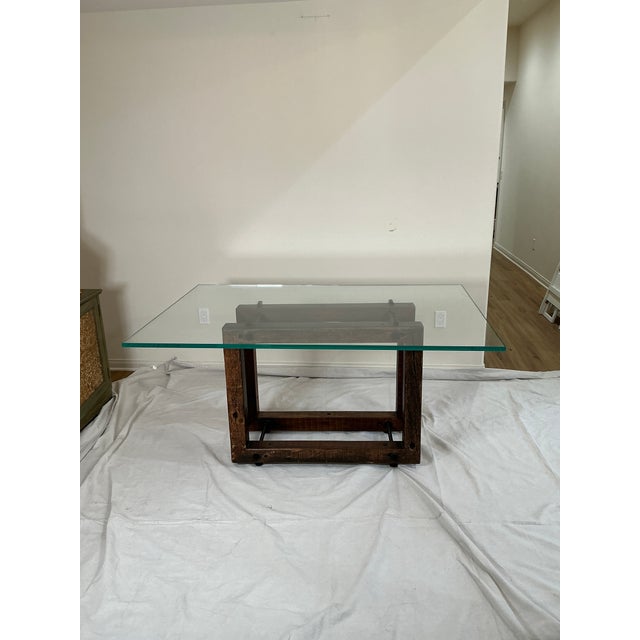 A striking modern dining table featuring a thick clear glass top set on a substantial solid wood base. The design blends...