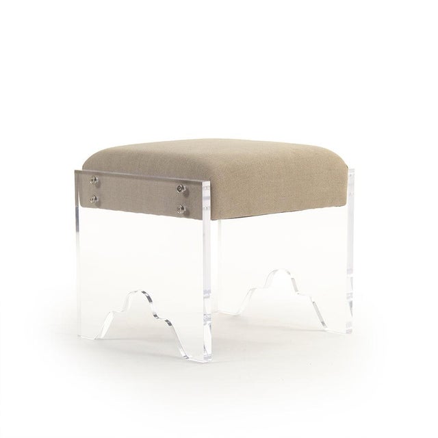 The Addie Acrylic Stool from Zentique is a modern vanity stool with a tan linen padded seat on a 1" thick clear acrylic...