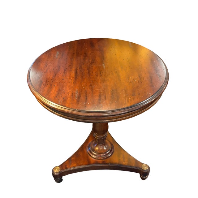 Round traditional-style occasional table crafted with a warm cherry or mahogany wood finish, featuring a molded circular...