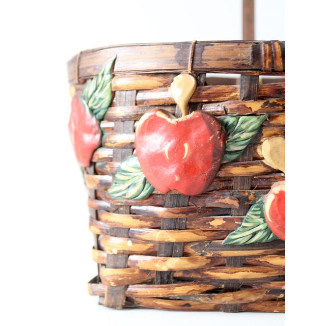 This vintage woven basket features dimensional red apples and painted green leaves against a dark brown woven ground. The...