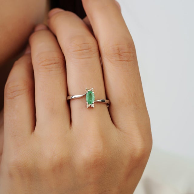 This elegant 925 sterling silver ring features a 0.57-carat natural oval emerald measuring 4 x 6 mm, beautifully framed by...