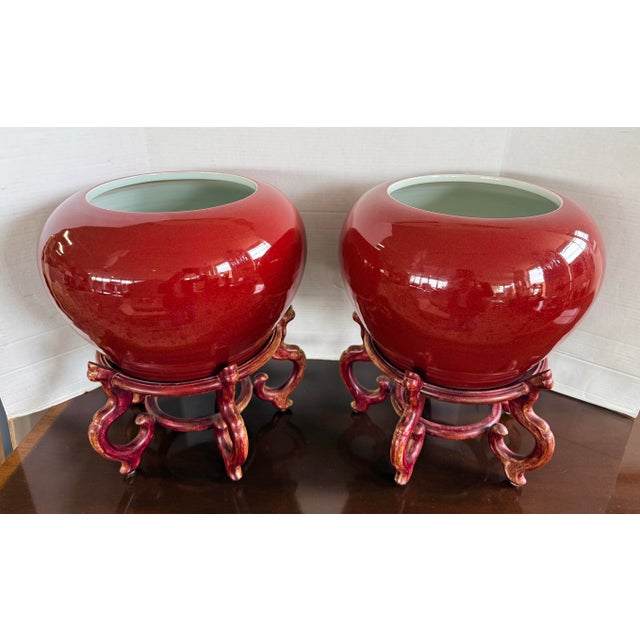 A striking pair of Chinese porcelain jardinieres in a rich oxblood glaze, presented with carved wooden display stands....