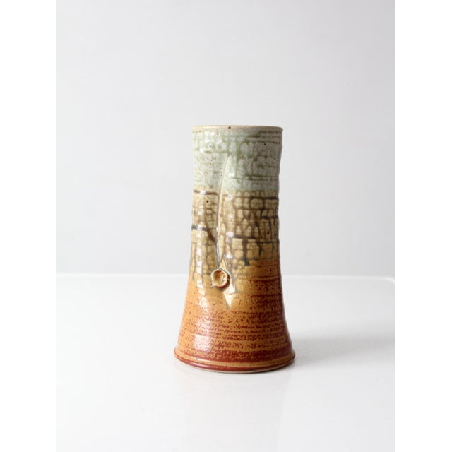 A vintage handmade studio pottery vase with a softly tapered silhouette and a layered glaze in earthy tones of rust, tan,...