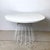 A round white laminate dining table with a Knoll-style wire base — steel rods radiating outward and downward from a...