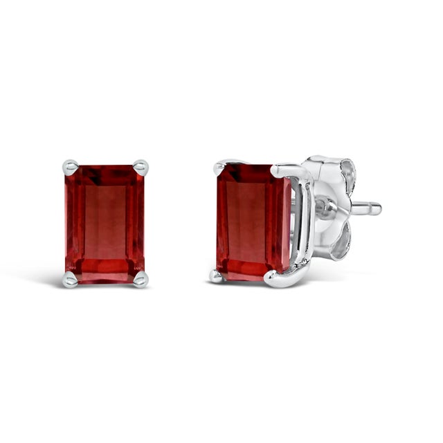 Immerse yourself in the timeless elegance of these stud earrings, each boasting a lustrous 6x4mm emerald-cut red garnet,...