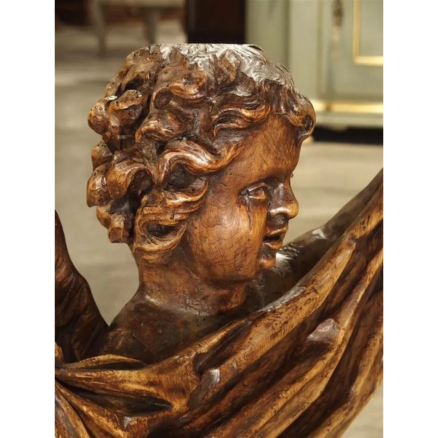 This hand carved seated cherub is of a nice size at nearly 23 inches tall. The cherub is holding a piece of draped cloth...