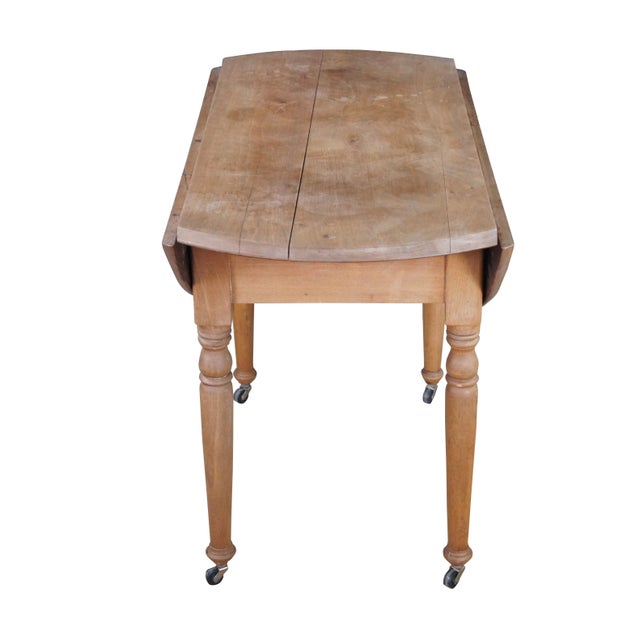 Early 20th Century Farmhouse Pine Drop Leaf Table. Features an oval top over turned legs with casters for ease of...