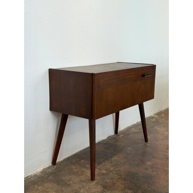 This compact entry table features a clean silhouette elevated by slender tapered legs. A drop-down door reveals a spacious...