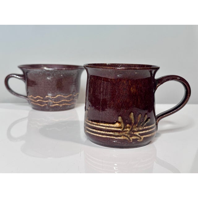 These two handcrafted ceramic mugs, one a large cocoa cup and the other a large coffee mug, bear the distinctive style of...