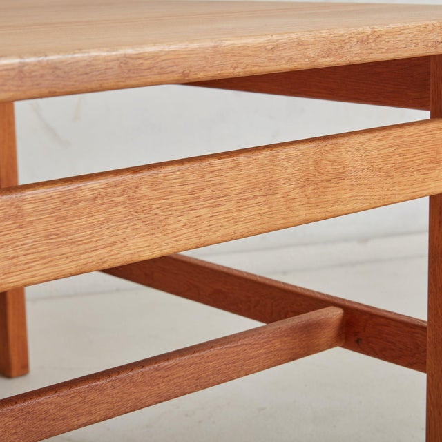 A charming, Mid-Century Modern coffee table constructed of solid wood in a warm, honey hue. The square surface is composed...