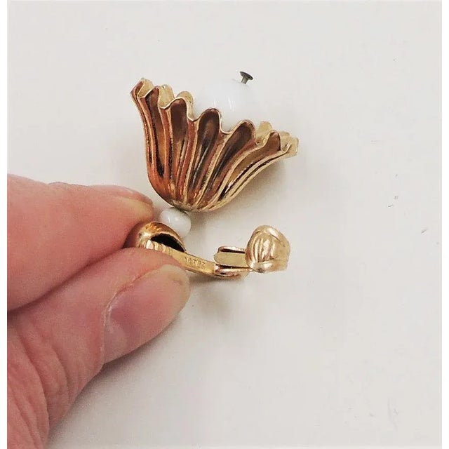 This is part of Chairish’s Costume Jewelry assortment. 1950s goldtone white resin bell clip earrings which chime...