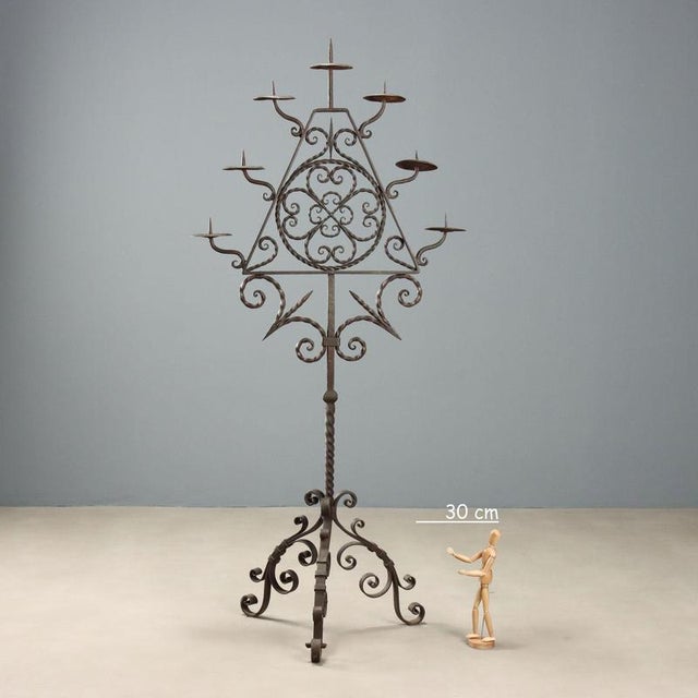 Wrought iron torch holder with seven flames. Tripod base and decoration of scrolls, spikes, and stylized flowers in the...
