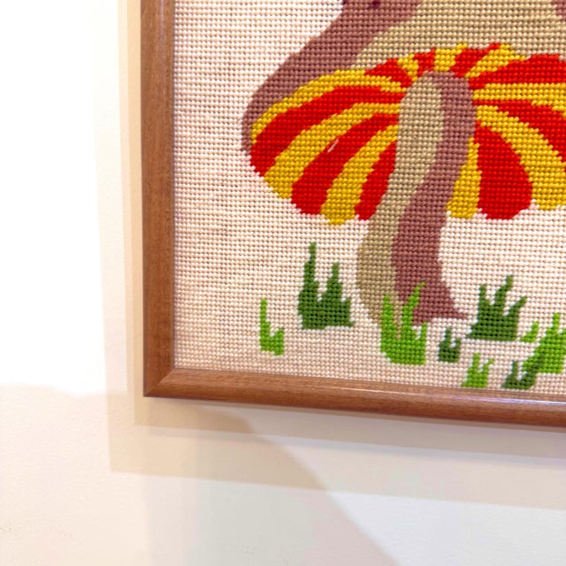 Here we have a framed piece of cross-stitch art featuring a brightly colored orange and yellow mushroom and a ladybug. The...