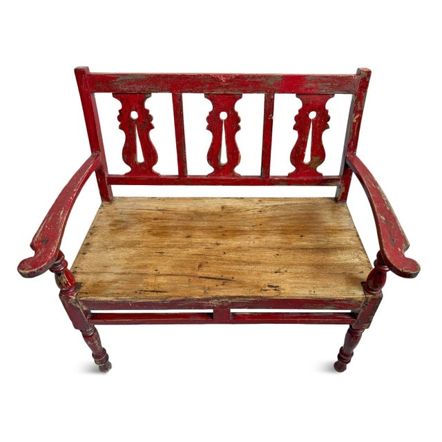 Vintage small teak hall bench from India with red painted and carved back, arms, and legs. Natural wood tone seat....