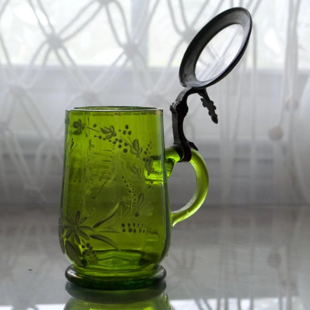 Charming late 19th-century German enameled glass syrup pitcher featuring a rich green glass body with hand-painted...