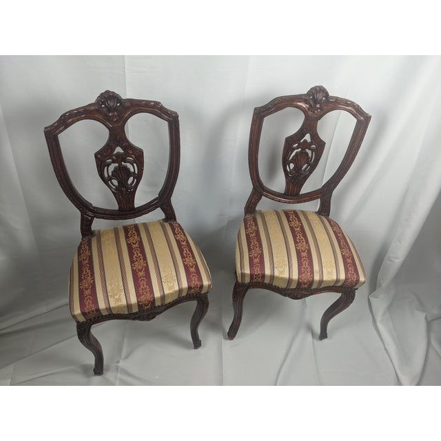 An elegant pair of French Louis XV style side chairs featuring hand-carved shell crests, pierced splat backs, and graceful...
