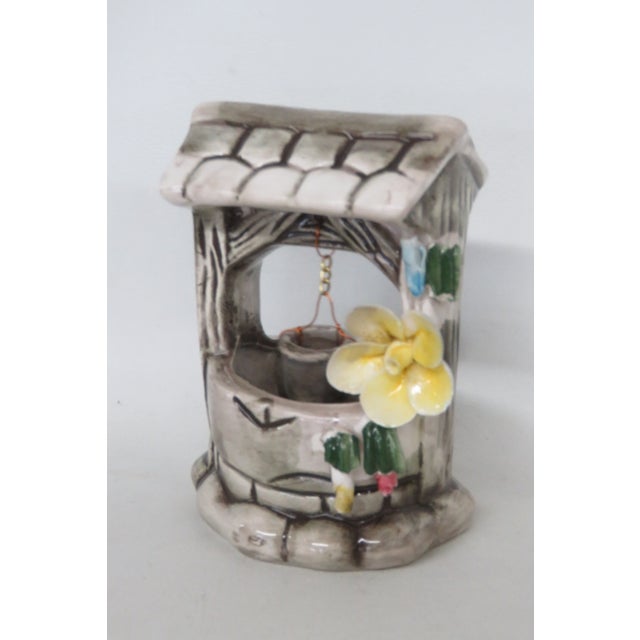 resemble stone texture, which is accented with lovely pink, yellow, and blue blossoms. There is a little bucket hanging by...