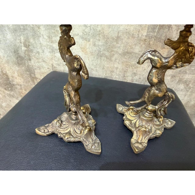 A brass candlestick pair modeled as rearing horses, each rising from a shaped base with a small turned support, scalloped...