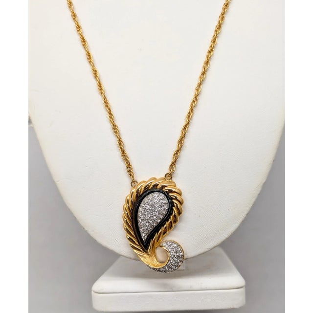 Goldtone paisley shaped pendant with pavé round clear rhinestones in the center with a black resin? border and more pavé...