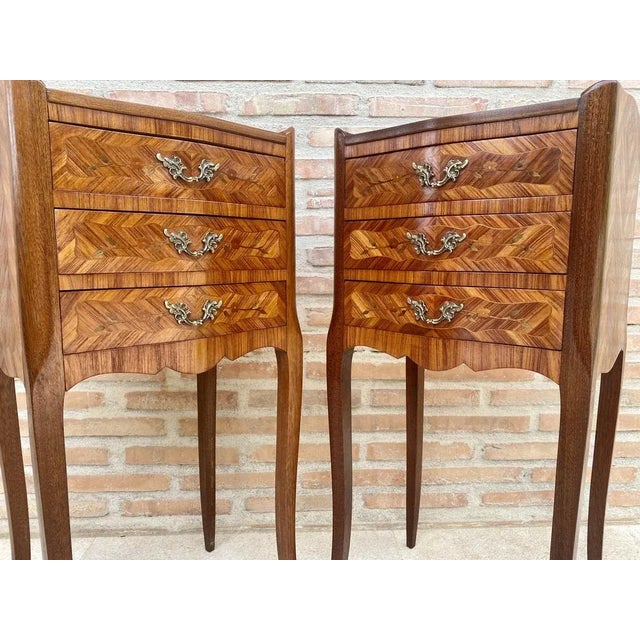 A rather elegant pair of tulipwood inlaid nightstands with floral marquetry on top and three drawers. Each drawer has its...