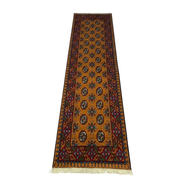 A warm terracotta-ochre field gives this runner its distinctive color. Two rows of repeating octagonal gul motifs run its...
