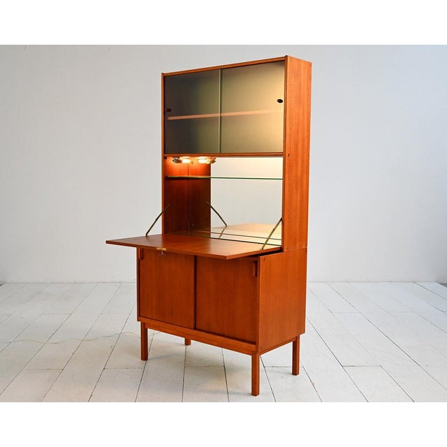 Teak bookcase with sliding lower doors, smoked glass display case at the top, and a drop-leaf door with an illuminated...