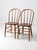 This is a pair of vintage wood dining chairs. The Windsor style farmhouse chairs feature round spindle backs and splay legs.