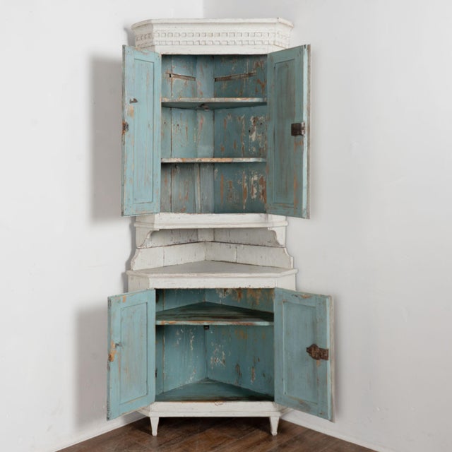19th century Swedish corner cabinet crafted in pine. The cabinet features a newer layered white painted finish with gray...