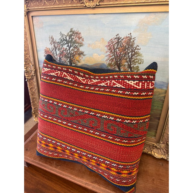 The pillow features a traditional, handwoven design with geometric patterns and vibrant colors like red, yellow, white,...