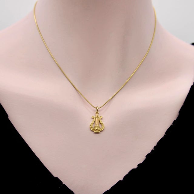 This is part of Chairish’s Fine Jewelry assortment. This 14k gold pendant is shaped like a musical lyre and inscribed with...