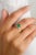 This exquisite wedding ring features a stunning 0.08 carat pear-cut green emerald, complemented by shimmering diamonds...