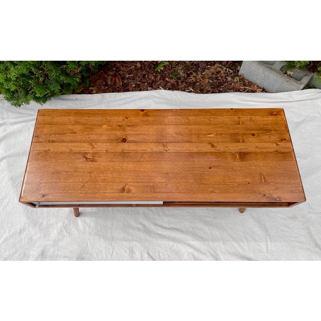 Vintage Mid-century modern coffee table features a chestnut pine wood frame, two white sliding doors, and tapered legs....