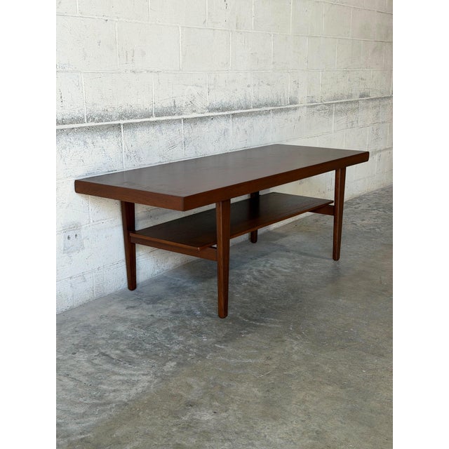 This long rectangular coffee table features a minimalist profile defined by clean lines. A built-in lower shelf offers a...