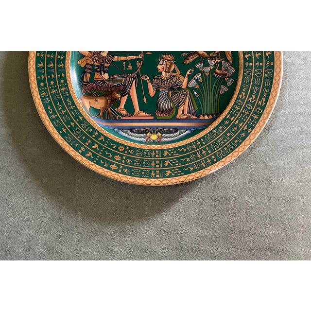 A vintage green & gold Egyptian Revival gold trimmed plate featuring a colorful hunting scene with a hieroglyphic border.