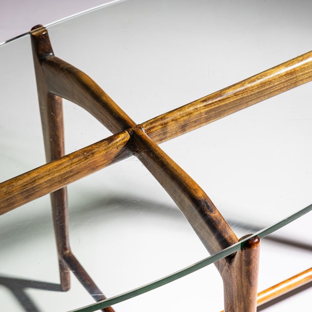 Oval coffee table featuring an elegant four-legged walnut base with an X-shaped stretcher. The glass tabletop adds a light...