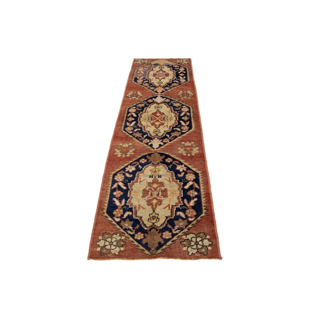 A beautiful vintage Turkish runner featuring a red-rust field decorated with a tribal traditional medallion design that...