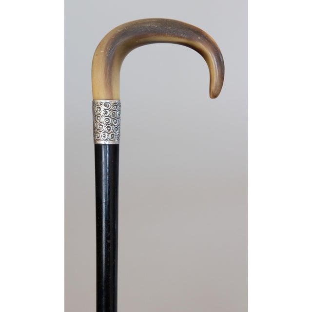 A superb antique English walking stick with an ebonized wood shaft, antler horn handle, and sterling silver collar. No...