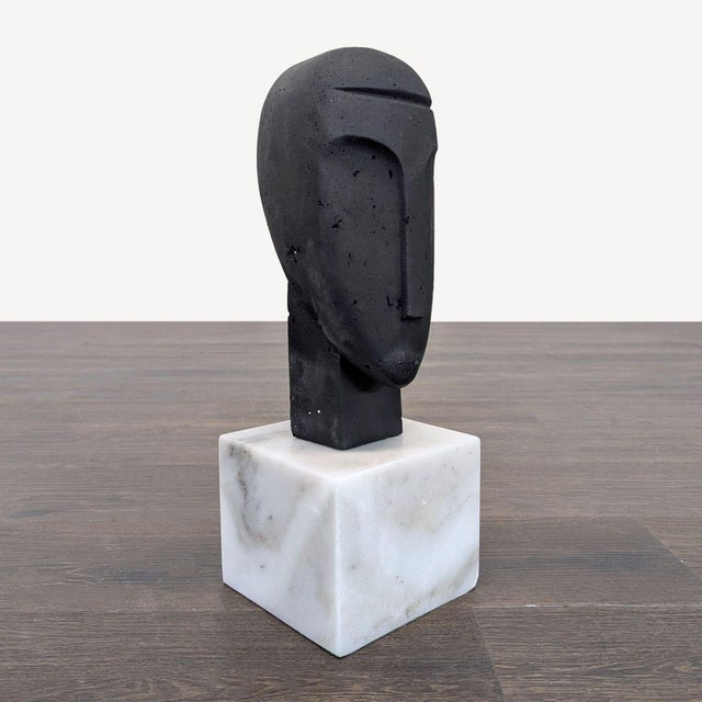 This sculpture features an abstract face design, crafted with a smooth finish and set on a solid white marble base. Its...