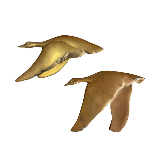 A striking pair of vintage solid brass flying bird wall hangings in a sleek Mid-Century Modern design. Depicting two geese...