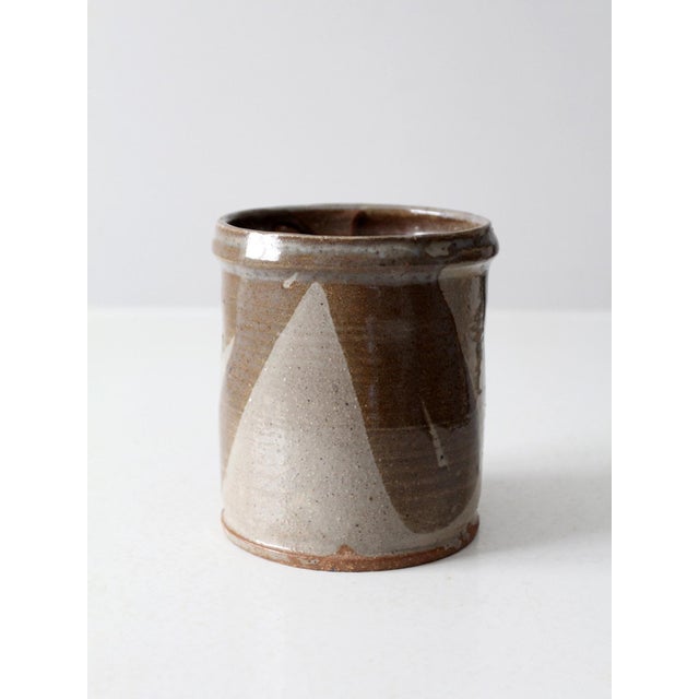 This vintage studio pottery crock features a sweeping taupe and brown glaze with a dynamic, fluid design. The handmade...