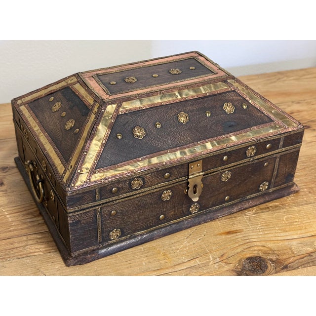 Vintage heavy wood box with brass clasp to front and rounded brass handles to each end. Features a decorative overlay of...