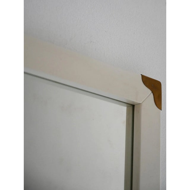 Scandinavian mirror from the 1950s, with a white lacquered frame and refined brass details at the corners. Original...