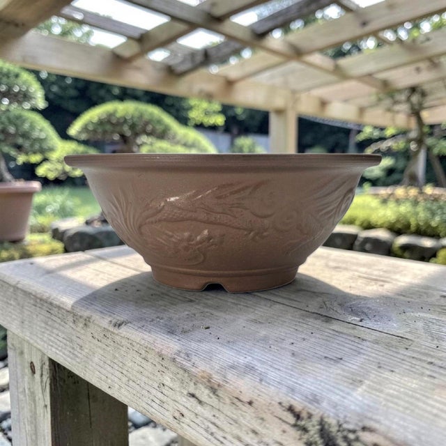Large Japanese-style bonsai pot executed in unglazed brown stoneware with molded dragon relief decoration. The round basin...