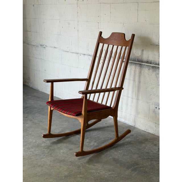 This rocking chair In style of Henning Kjærnulf features a high spindle backrest and distinctive contoured crest rail. Its...