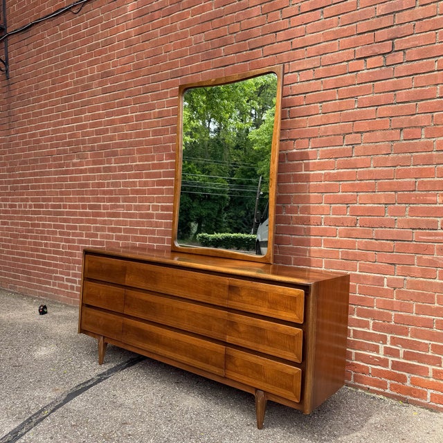 Long walnut lowboy dresser by American of Martinsville with nine drawers and original mirror. Features softly beveled...